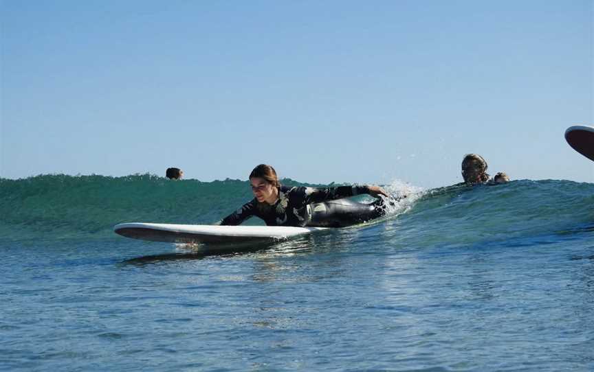 Student getting pushed into a green unbroken wave during a surf lesson.