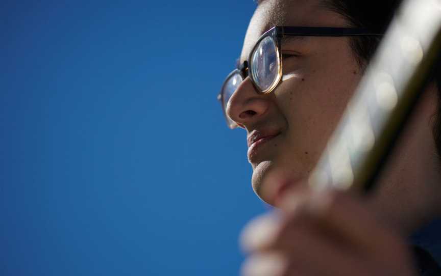 Photo of a man's face with glasses against a blue sky, and in the foreground the fretboard of a guitar.