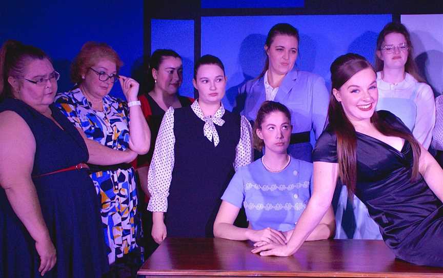 Hedy LaRue (Breanna Redhead, on desk) feels the wrath of other women in the corporate world as part of How to Succeed in Business Without Really Trying.