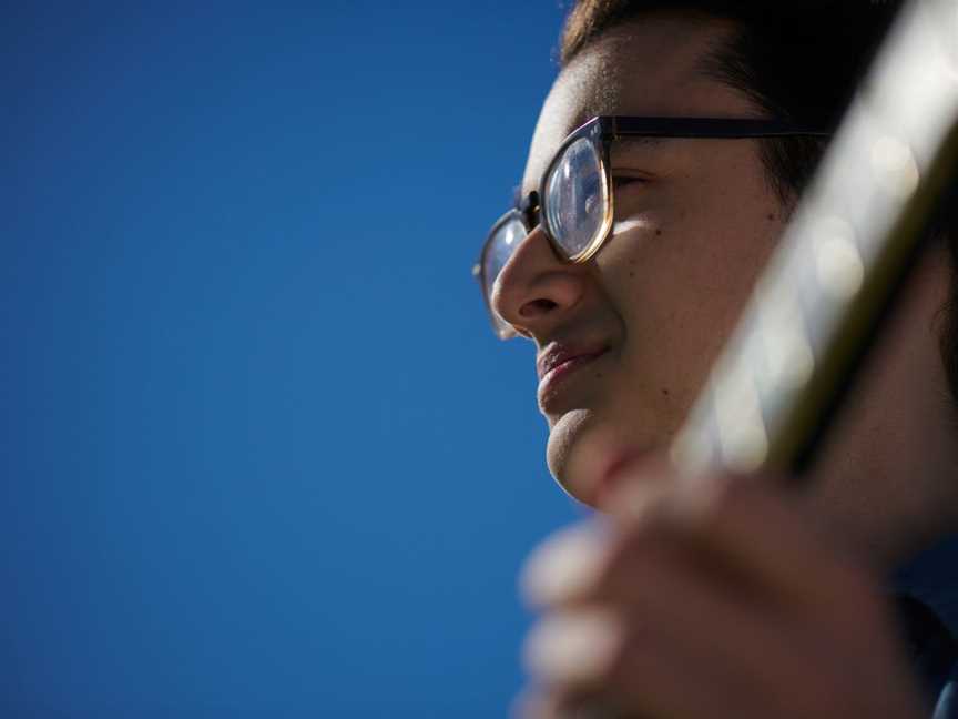 Perspective below a glasses-wearing man's face, who is holding a guitar