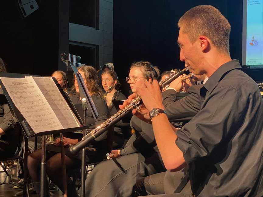 Musicians wearing black are performing on a stage with music stands in front of them