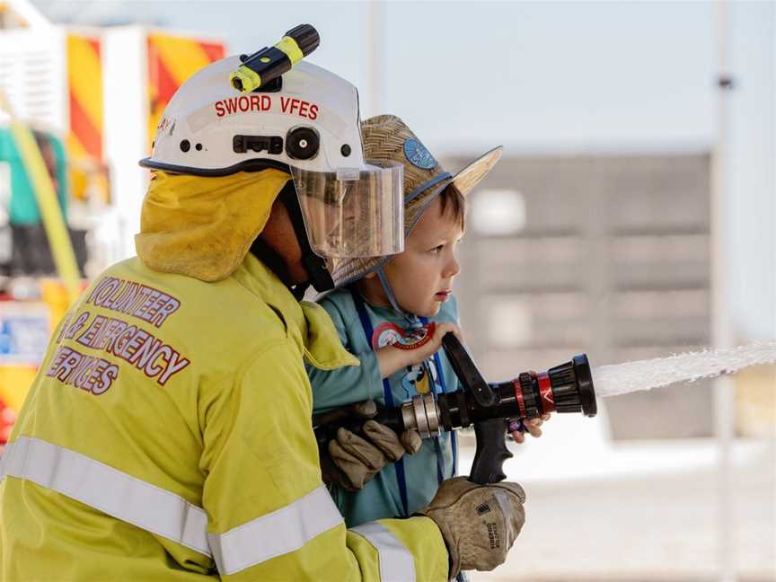 Child spraying hose with Volunteer Firefighter