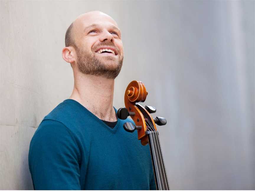 Person in a blue jumper stands looking to the sky. The next of a cello is visible.